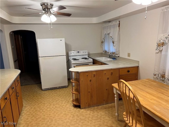 kitchen featuring arched walkways, brown cabinets, a sink, white appliances, and a peninsula