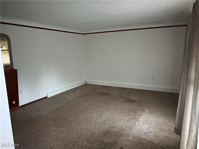 spare room featuring arched walkways, carpet flooring, and baseboards