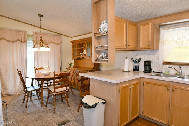 kitchen with a textured ceiling, a peninsula, a sink, light countertops, and hanging light fixtures