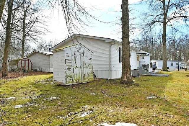 view of side of property with a shed, a lawn, central AC, and an outbuilding