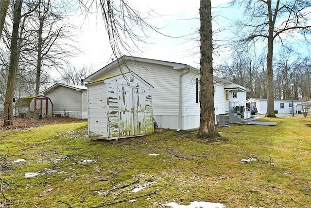 rear view of house featuring an outbuilding, a lawn, central AC unit, and a shed