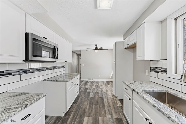 kitchen featuring dark wood-style floors, stainless steel microwave, white cabinets, and light stone counters