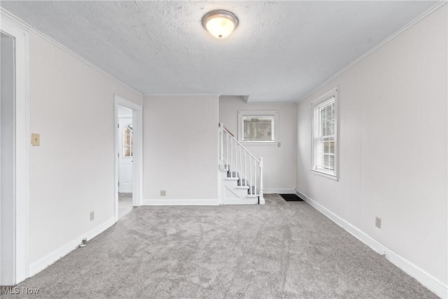 empty room featuring a textured ceiling, carpet floors, stairway, and crown molding