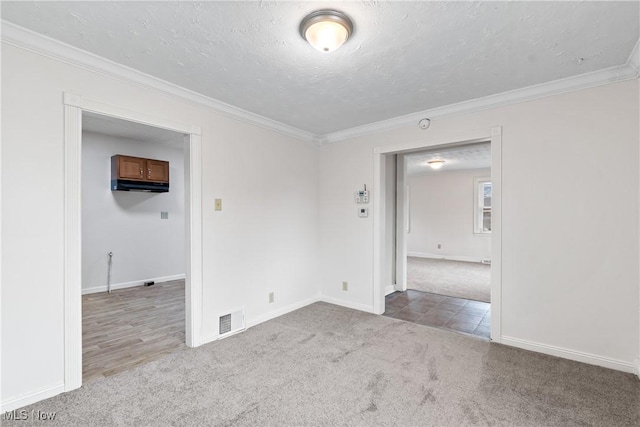 carpeted spare room featuring a textured ceiling, ornamental molding, visible vents, and baseboards