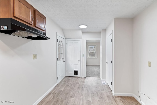 corridor with light wood-style flooring, visible vents, baseboards, and a textured ceiling