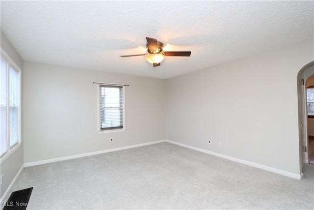 spare room with light carpet, visible vents, arched walkways, a ceiling fan, and a textured ceiling