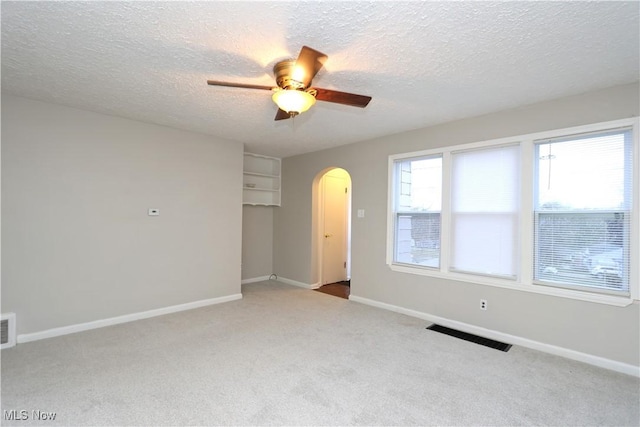 carpeted spare room featuring visible vents, arched walkways, ceiling fan, and baseboards