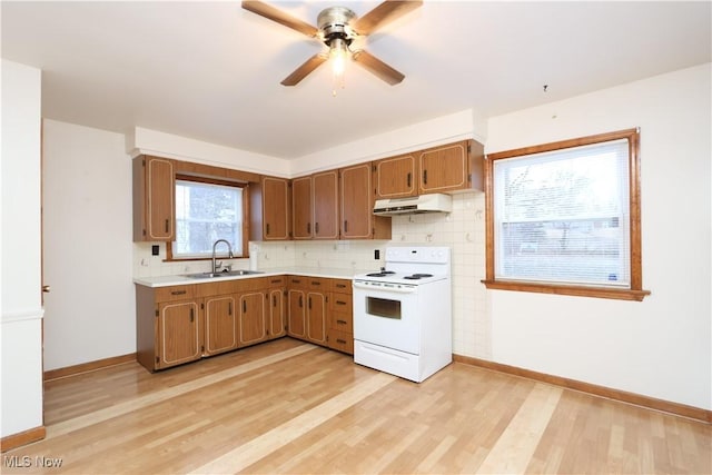 kitchen featuring white electric range oven, light wood-style floors, light countertops, under cabinet range hood, and a sink