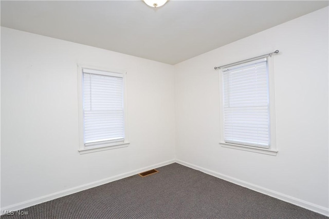 unfurnished room featuring baseboards, visible vents, and dark carpet