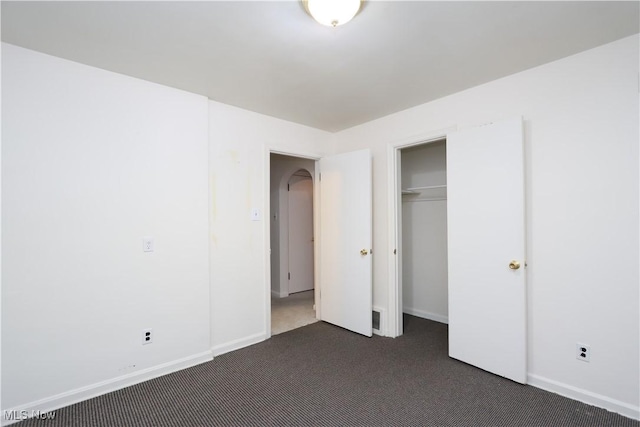 unfurnished bedroom featuring arched walkways, carpet flooring, and baseboards