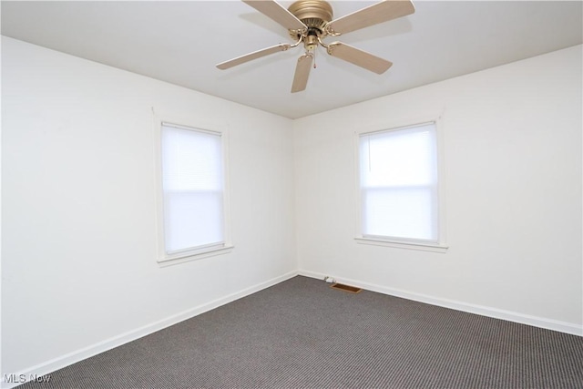 spare room with baseboards, visible vents, dark carpet, and ceiling fan
