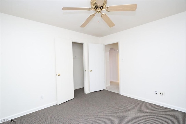 carpeted empty room with a ceiling fan, arched walkways, and baseboards