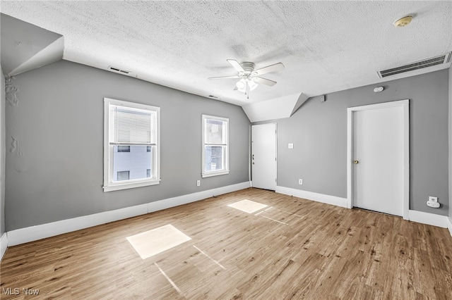 spare room with visible vents, a ceiling fan, wood finished floors, vaulted ceiling, and a textured ceiling