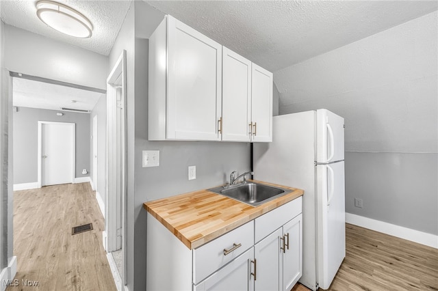 kitchen featuring lofted ceiling, a sink, visible vents, white cabinetry, and light wood finished floors