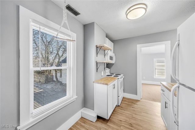 kitchen featuring visible vents, light wood-style flooring, white cabinets, a textured ceiling, and white appliances