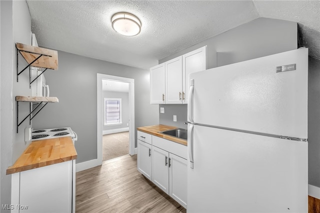 kitchen featuring wooden counters, a sink, freestanding refrigerator, and white cabinetry