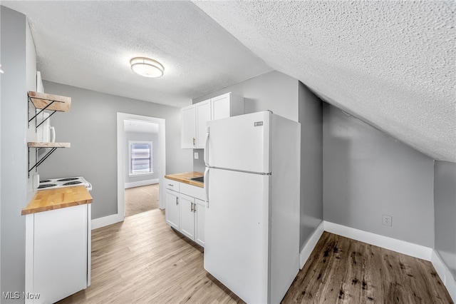 kitchen with light wood-style floors, butcher block counters, white cabinets, and freestanding refrigerator