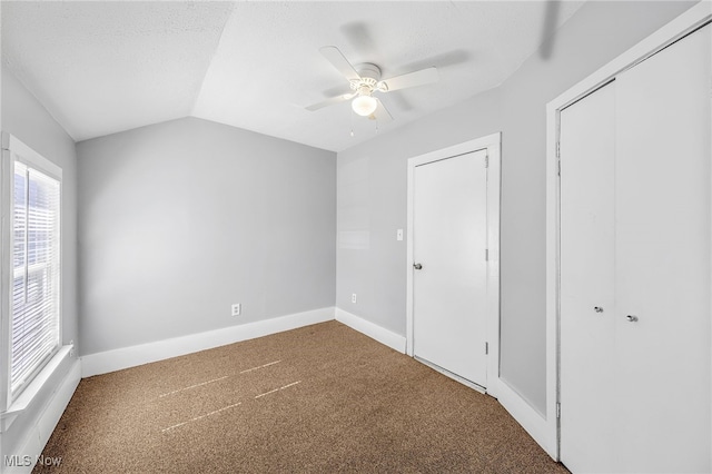 unfurnished bedroom featuring carpet floors, lofted ceiling, a closet, ceiling fan, and baseboards