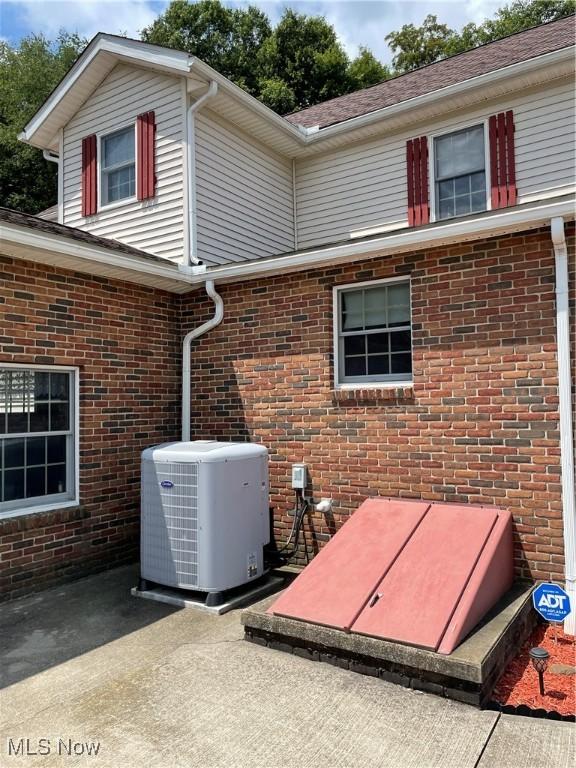 exterior details featuring gutters, cooling unit, a bulkhead entry, a downspout, and brick siding