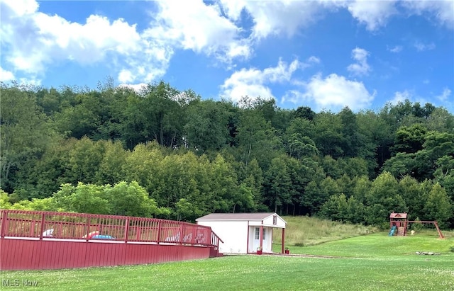 view of yard with a playground, a storage shed, an outdoor structure, and a wooded view