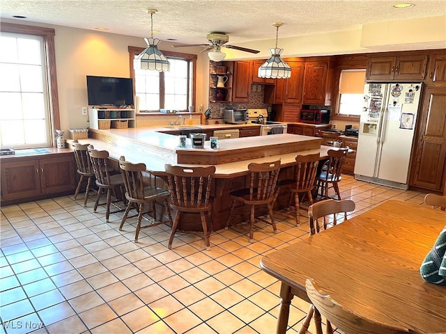 kitchen featuring light tile patterned floors, a peninsula, white appliances, hanging light fixtures, and decorative backsplash