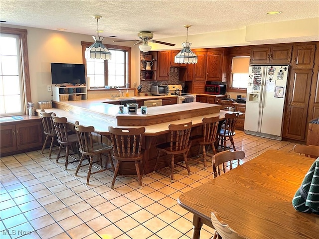 kitchen featuring pendant lighting, light tile patterned floors, decorative backsplash, white appliances, and a peninsula