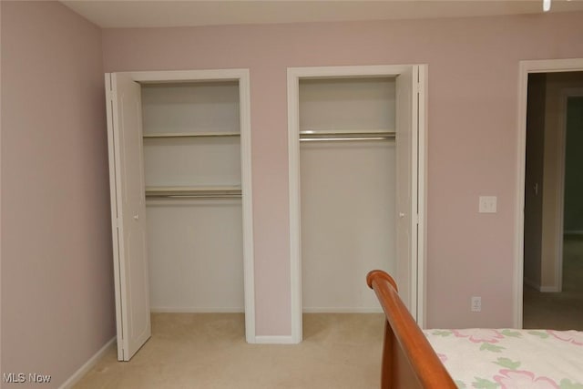 unfurnished bedroom with light carpet, baseboards, and two closets