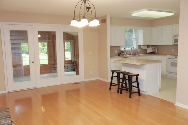 kitchen with white microwave, a breakfast bar, stove, a sink, and white cabinetry