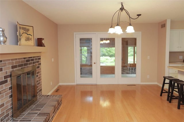 living area featuring a fireplace, visible vents, wood finished floors, a chandelier, and baseboards