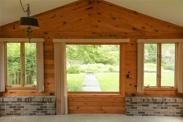 interior space featuring lofted ceiling, carpet floors, a wealth of natural light, and wooden walls