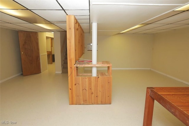 finished basement featuring stairway, baseboards, and a drop ceiling