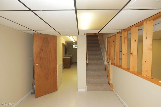 finished below grade area featuring stairs, baseboards, a drop ceiling, and tile patterned floors