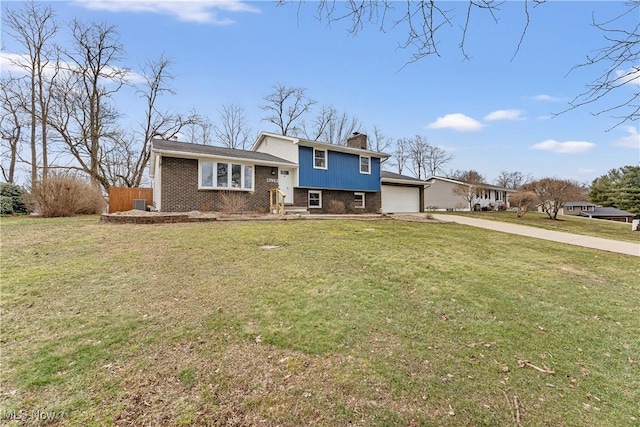 tri-level home with brick siding, a chimney, concrete driveway, an attached garage, and a front lawn