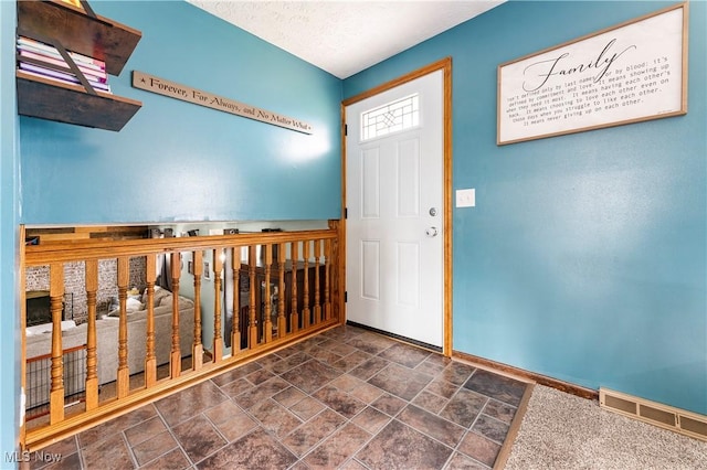 foyer with stone finish floor, baseboards, visible vents, and a textured ceiling