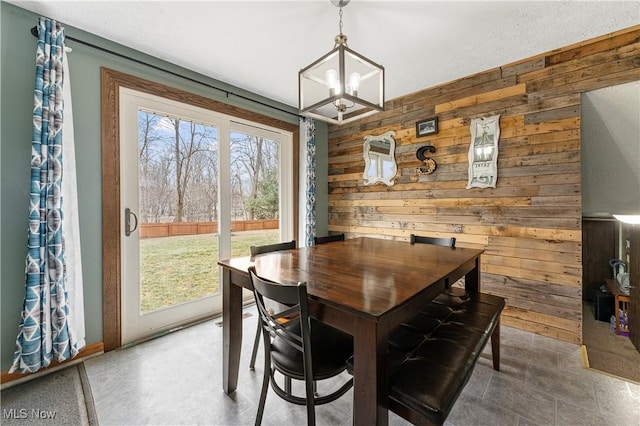 dining area with wood walls and an inviting chandelier