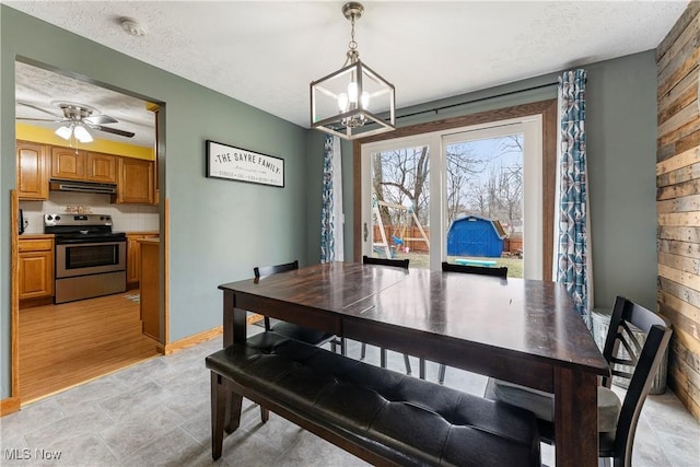 dining space featuring a textured ceiling, wood walls, and ceiling fan with notable chandelier