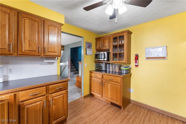 kitchen featuring brown cabinets, dark countertops, stainless steel microwave, and backsplash