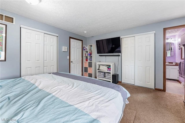 carpeted bedroom with connected bathroom, a textured ceiling, visible vents, and two closets