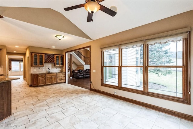 kitchen featuring baseboards, brown cabinetry, decorative backsplash, glass insert cabinets, and vaulted ceiling