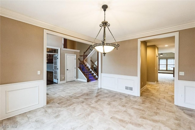 unfurnished dining area with crown molding, visible vents, a decorative wall, stairway, and wainscoting