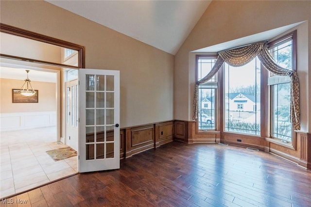 unfurnished room with dark wood finished floors, wainscoting, vaulted ceiling, french doors, and a decorative wall