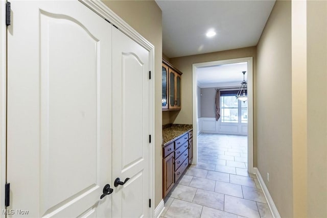 corridor with a wainscoted wall, ornamental molding, and light tile patterned flooring