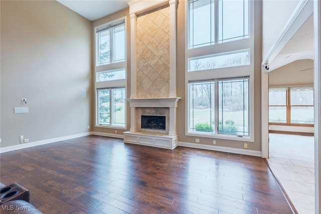 unfurnished living room featuring visible vents, baseboards, a fireplace with raised hearth, dark wood-style floors, and a high ceiling