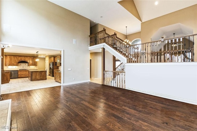 unfurnished living room featuring a chandelier, light wood-style flooring, a towering ceiling, baseboards, and stairway