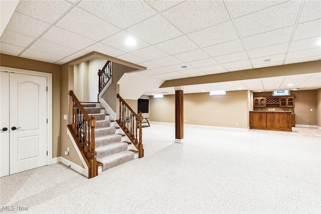 finished below grade area featuring stairs, a paneled ceiling, and baseboards