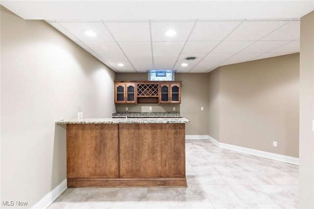 kitchen with a peninsula, baseboards, visible vents, and glass insert cabinets