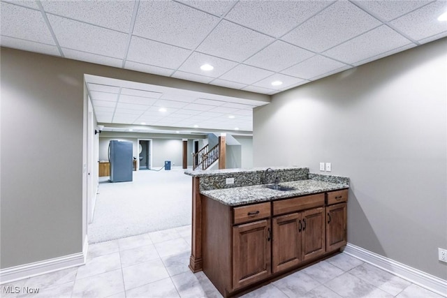 kitchen with light stone counters, a paneled ceiling, a sink, a peninsula, and baseboards