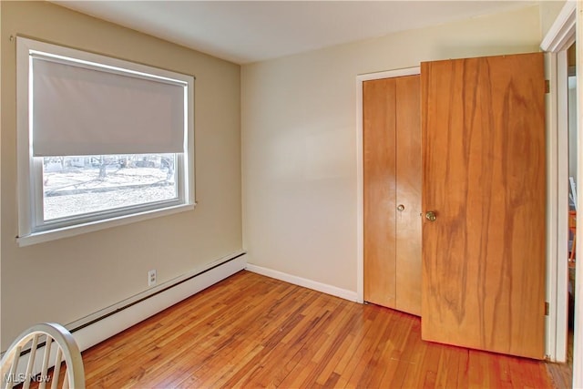 unfurnished bedroom featuring light wood-type flooring, baseboards, baseboard heating, and a closet