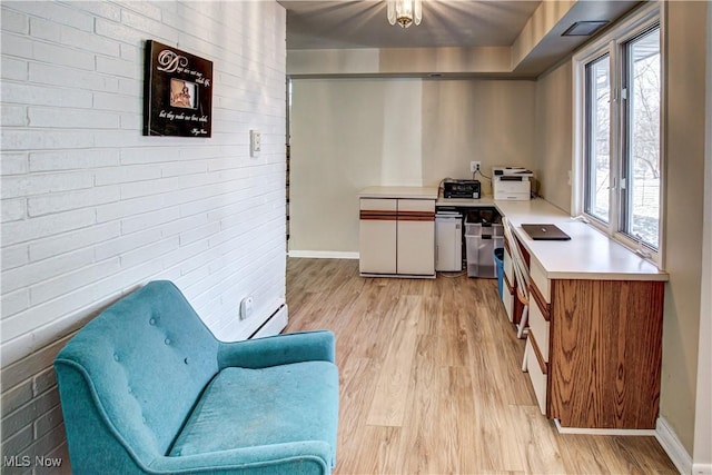 kitchen with light wood-type flooring, baseboards, light countertops, and brick wall