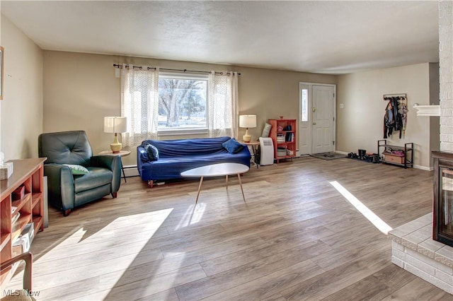 sitting room featuring a baseboard heating unit, a brick fireplace, baseboards, and wood finished floors